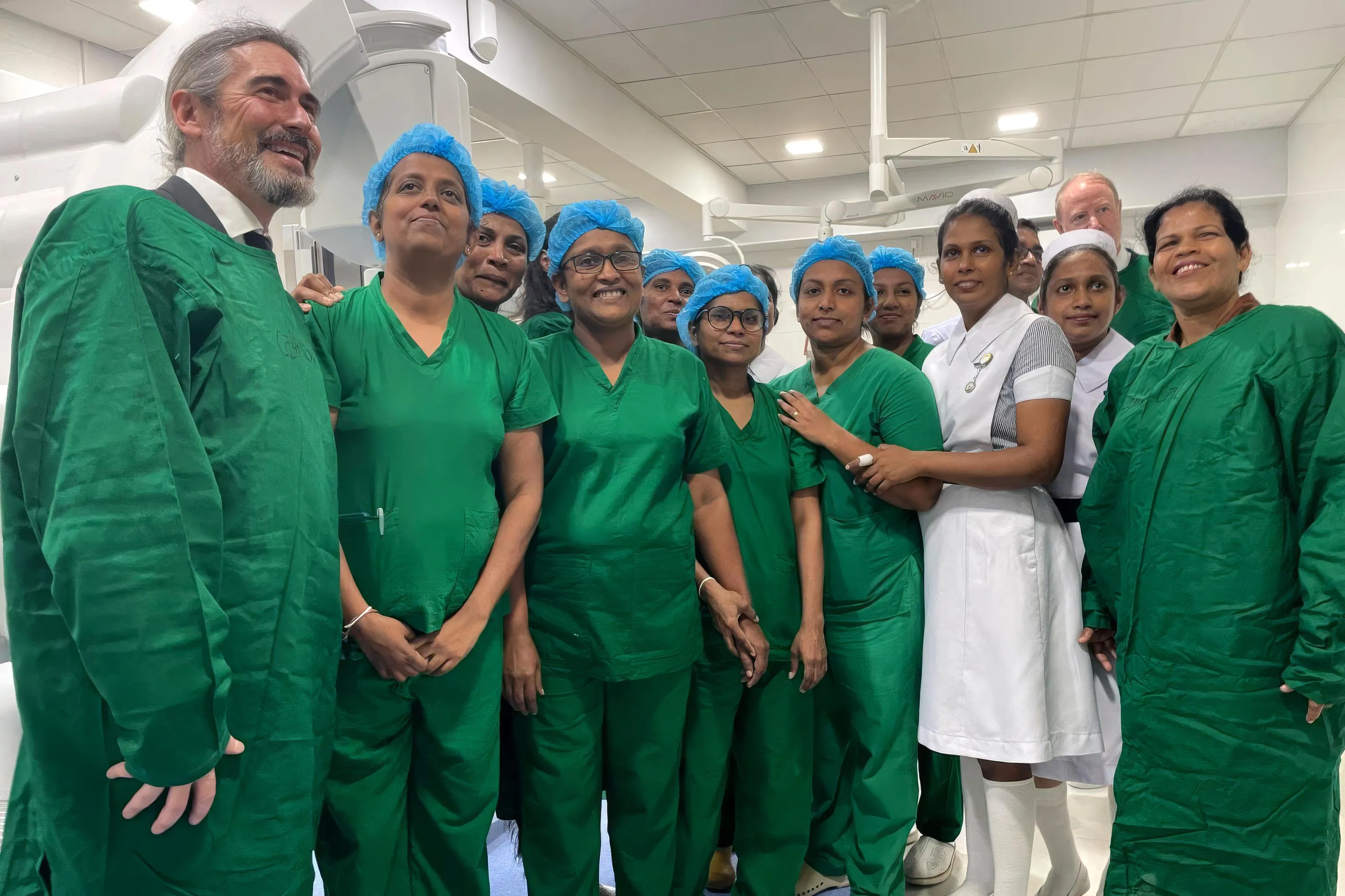 Un grupo numeroso de personal sanitario, la mayoría mujeres, con bata verde y gorro quirúrgico azul, posa sonriente en una sala de intervenciones del proyecto de la fundación en Sri Lanka.
