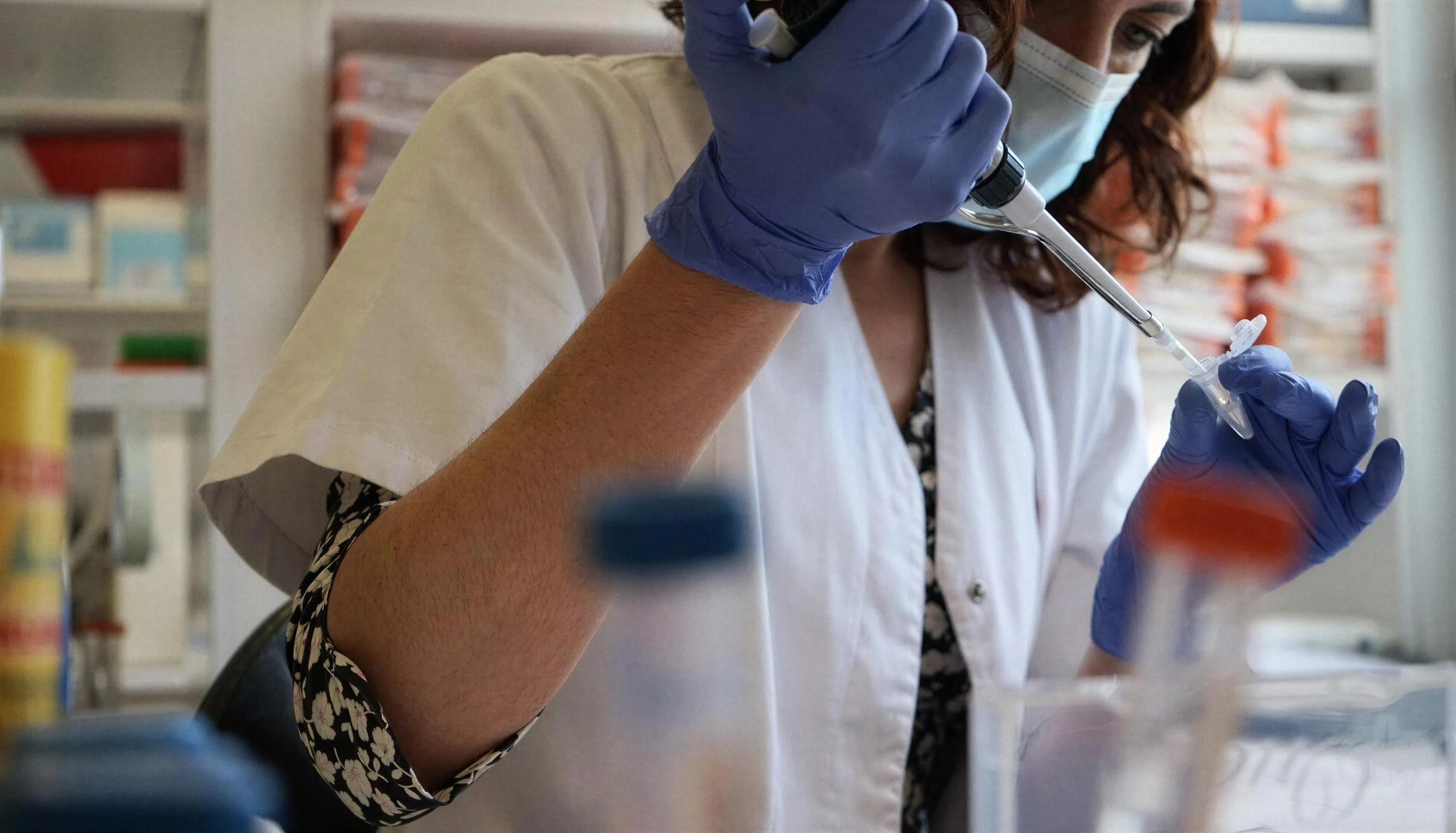 Una profesional con bata, mascarilla y guantes azules pipetea una muestra en un tubo en el laboratorio del hospital.