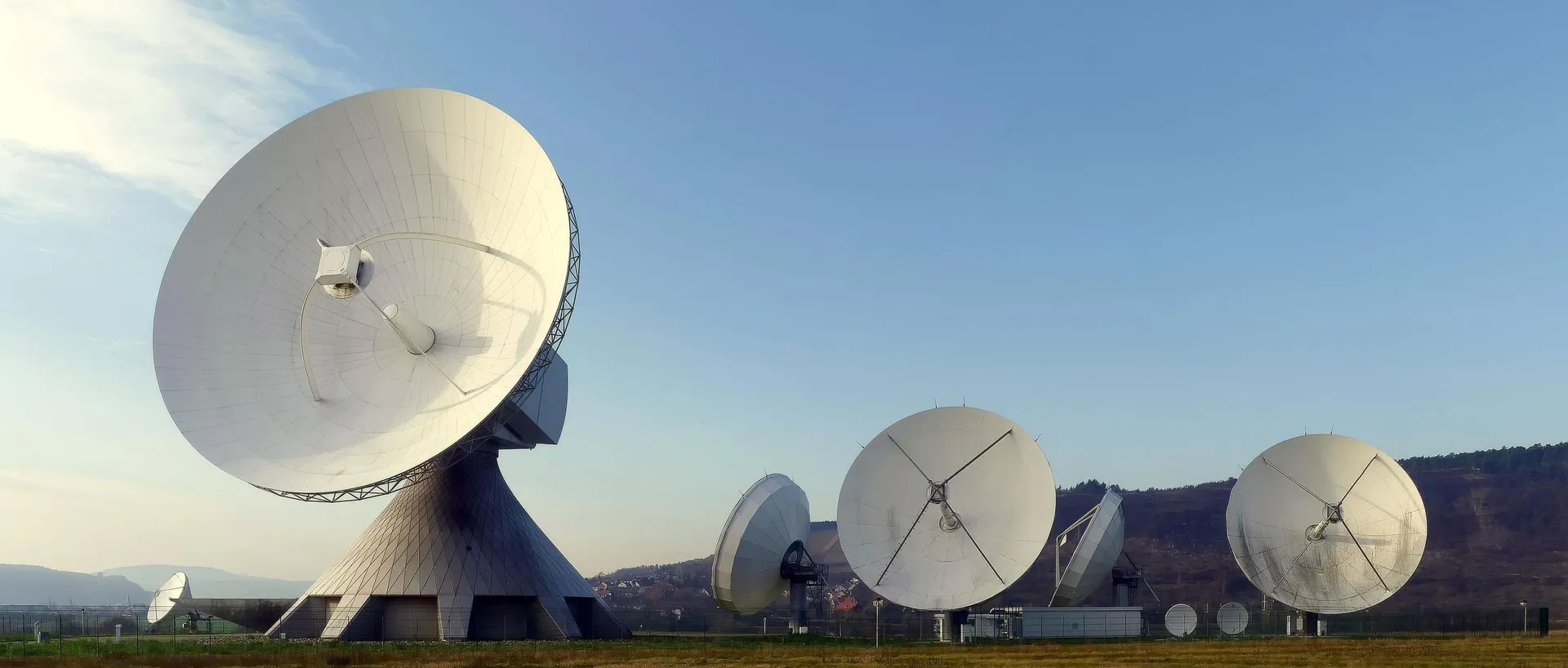Varias antenas parabólicas blancas de gran tamaño en una estación de seguimiento por satélite, bajo un cielo despejado, sin personas.