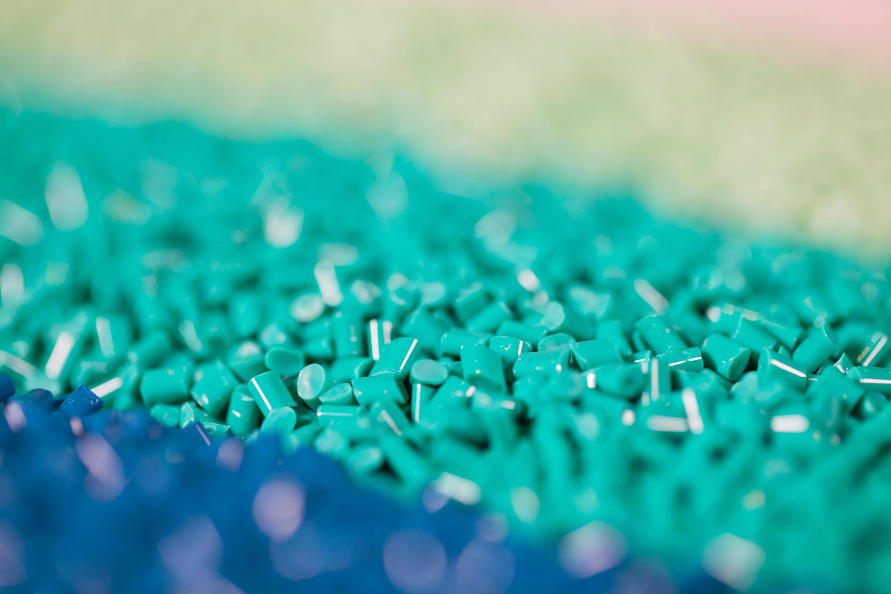 Primer plano de gránulos de plástico de color verde y azul sobre una superficie, el material que fabrica ELIX Polymers.
